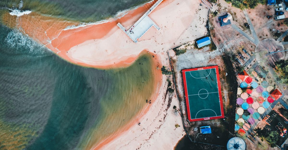 Stunning aerial shot of a beachside football court and colorful umbrellas.