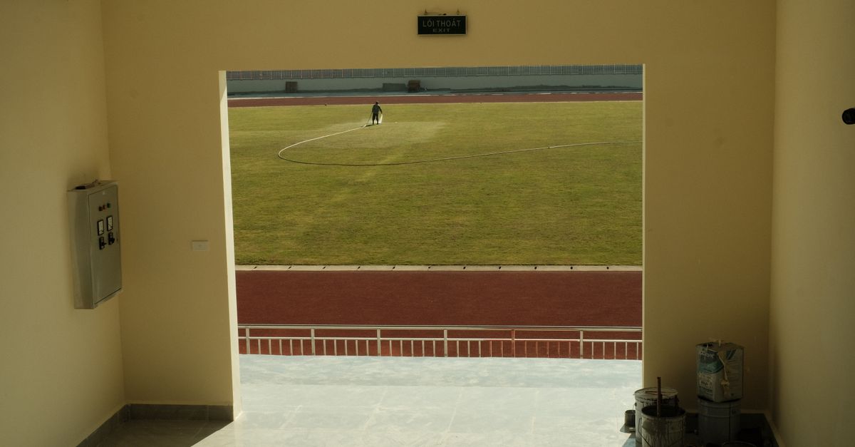 A sunlit view from an interior hallway looking out to a grass football pitch with a person working.
