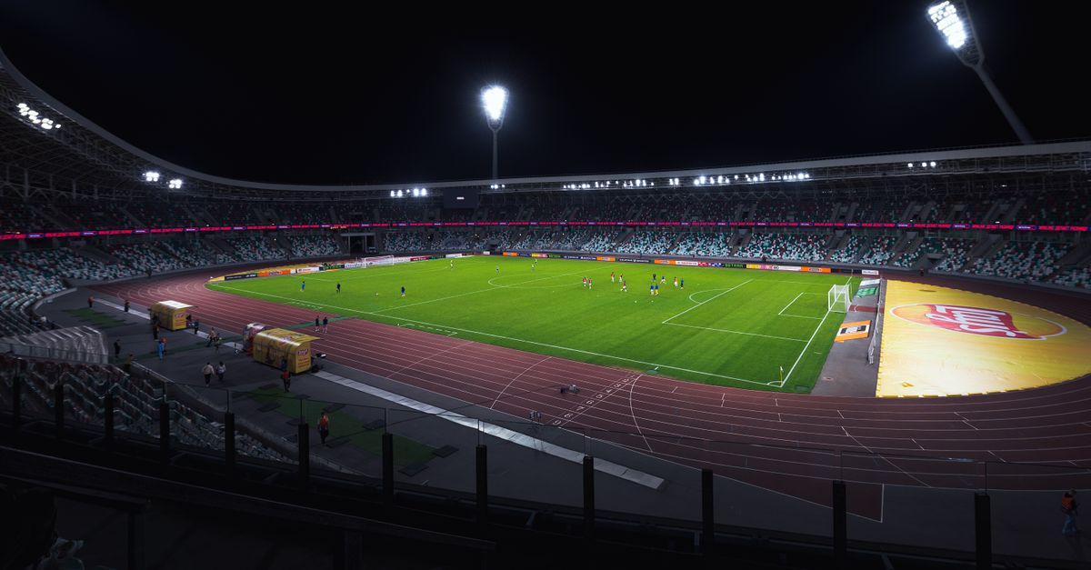 Brightly lit empty soccer stadium with green field under spotlights during night time.
