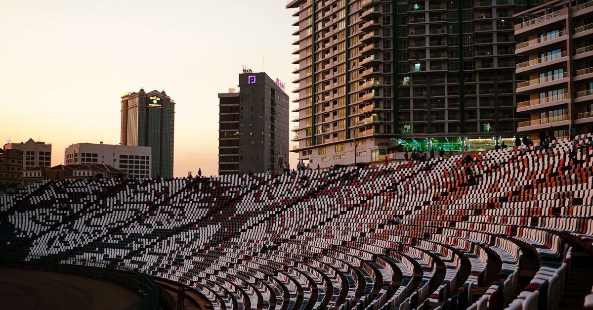 Curved stadium seats in Phnom Penh with city skyline at sunset. Modern architecture and vibrant colors captured.