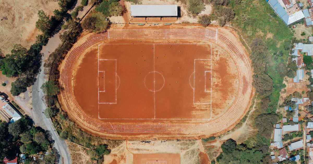 Aerial shot capturing a rustic football field and basketball court surrounded by natural scenery.