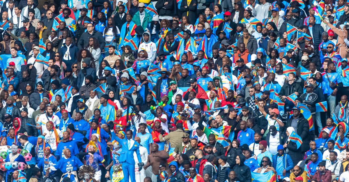 Packed stadium with diverse crowd waving Congolese flags, celebrating unity.