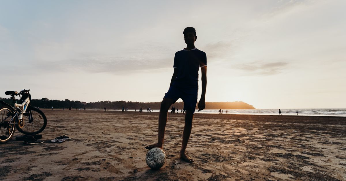 Silhouette of a man on a sandy beach with a soccer ball at sunset, showcasing leisure and recreation.