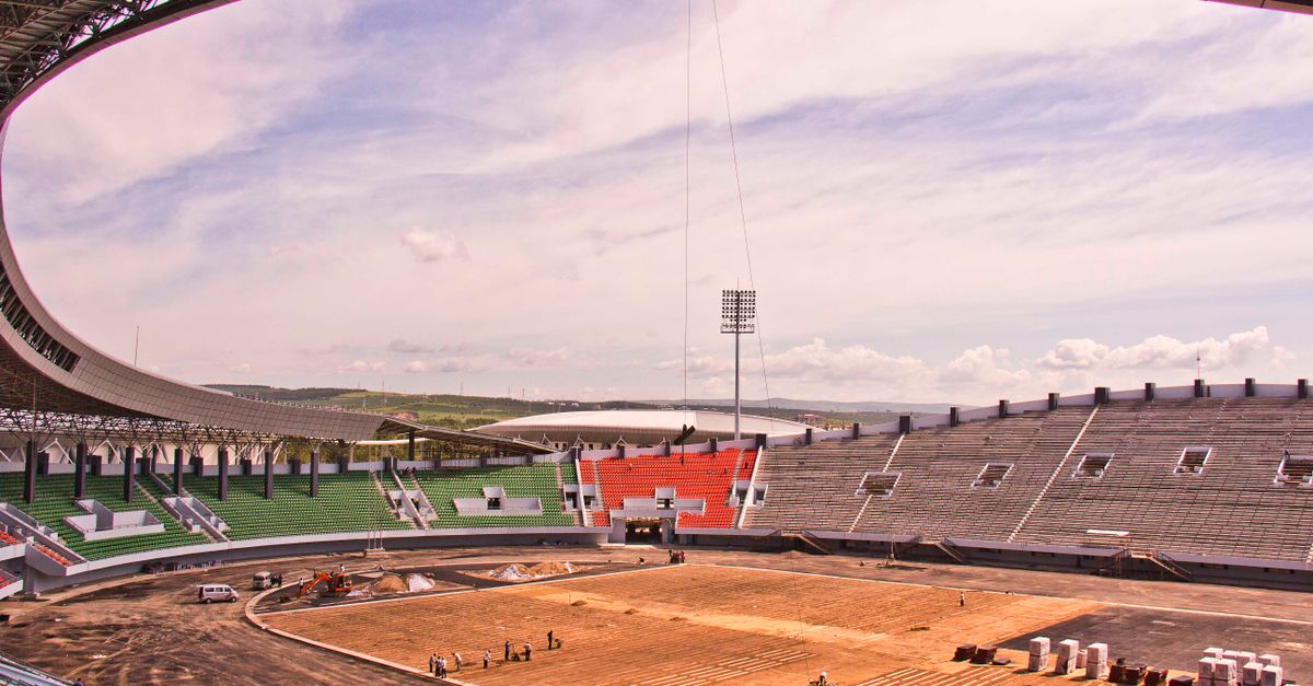 Wide-angle view of a stadium under construction, showcasing seating and a cloudy sky.